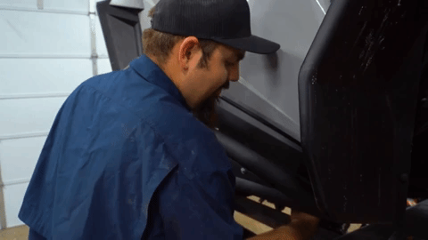 Braden finger-tightens a bolt under the body of the UTV.