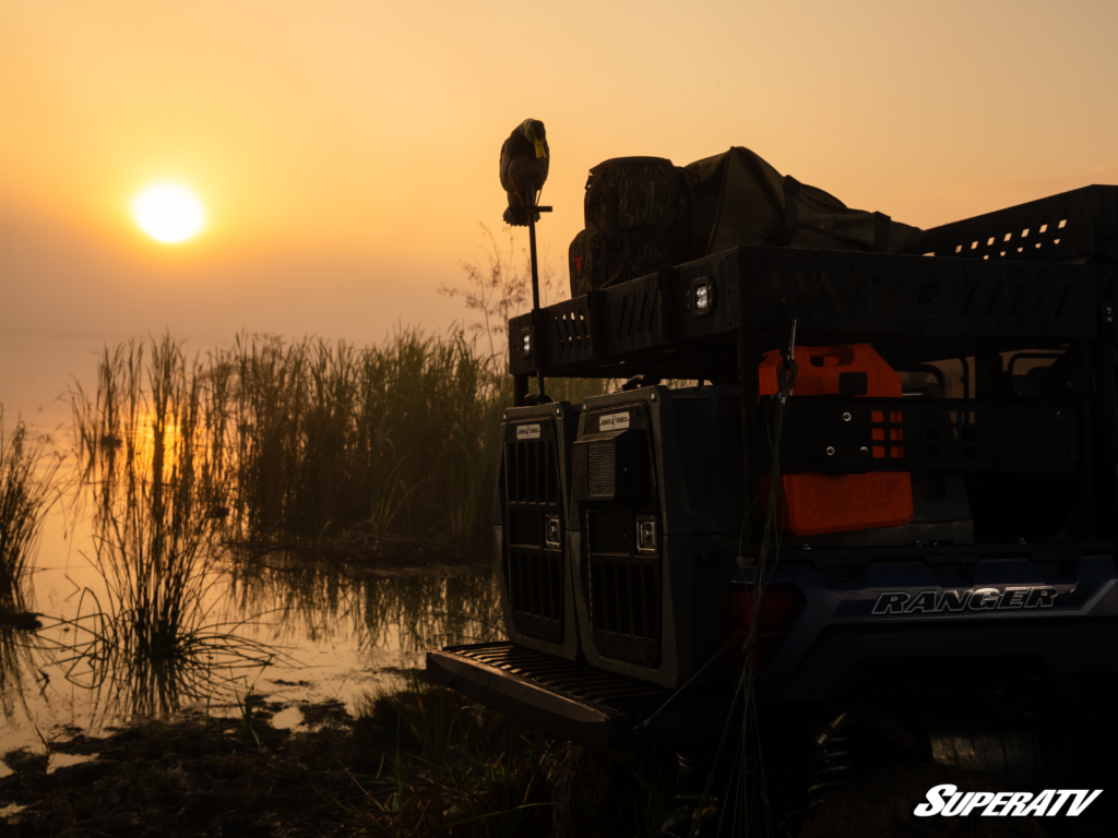 The sun is rising over a foggy swamp. A Polaris Ranger is parked at t he edge of the water.