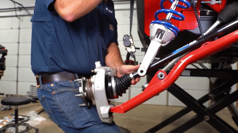 Braden braces the steering knuckle against his leg as he removes the strap from the upper A-arm.