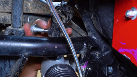 A hand reaches up in a tight space and inserts a bolt into a hole.
