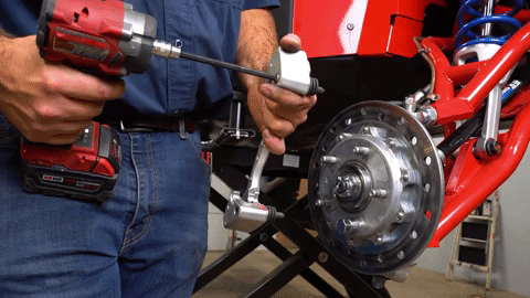 Braden uses a red Milwaukee drill to remove an allen-headed bolt from the caliper.
