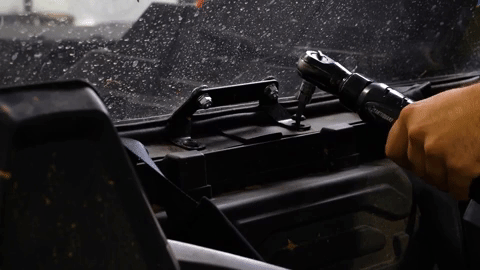 A hand uses a power drill to remove bolts from a bracket inside the cab of the side-by-side.