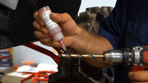 A hand squeezes a tube of red gel onto the tip of a drill bit.
