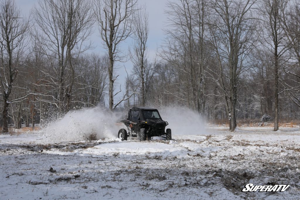 A Polaris RZR driving through the snow with a soft cab enclosure.