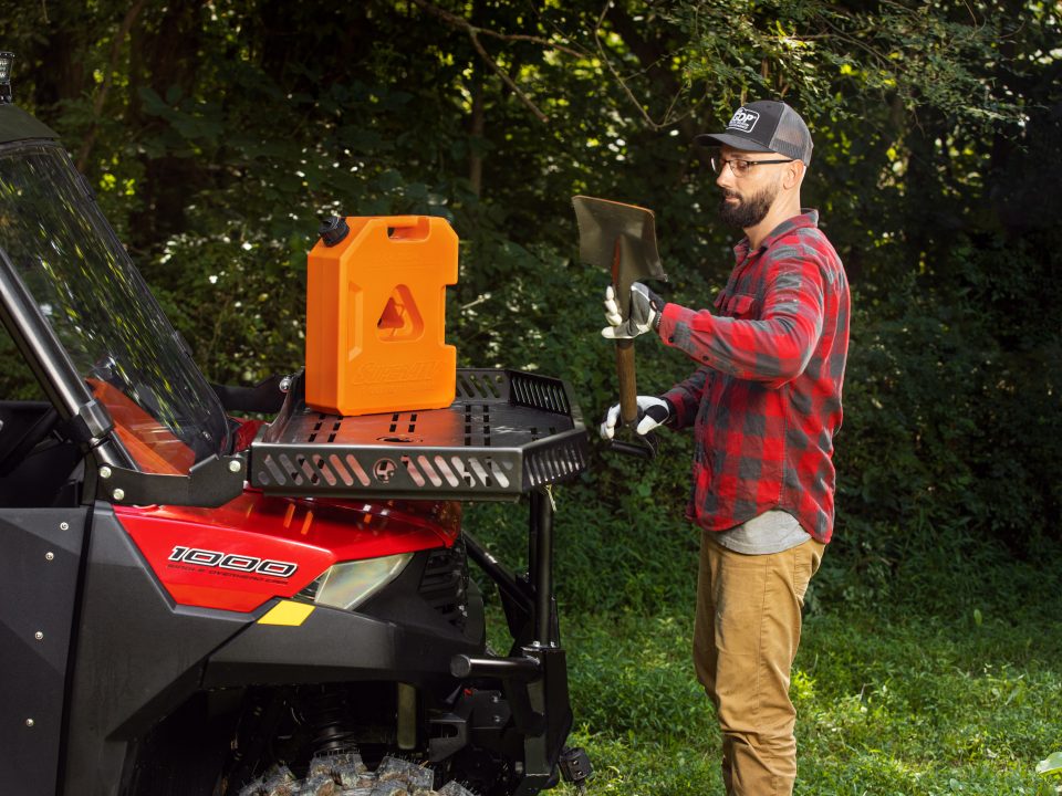 A man holds a shovel standing at a UTV. A gas can sits on a cargo rack.