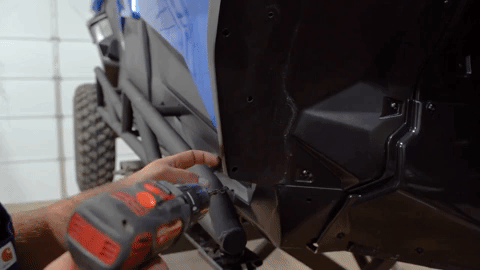 Braden uses a drill to make a hole in the OEM fender along the bottom left side.