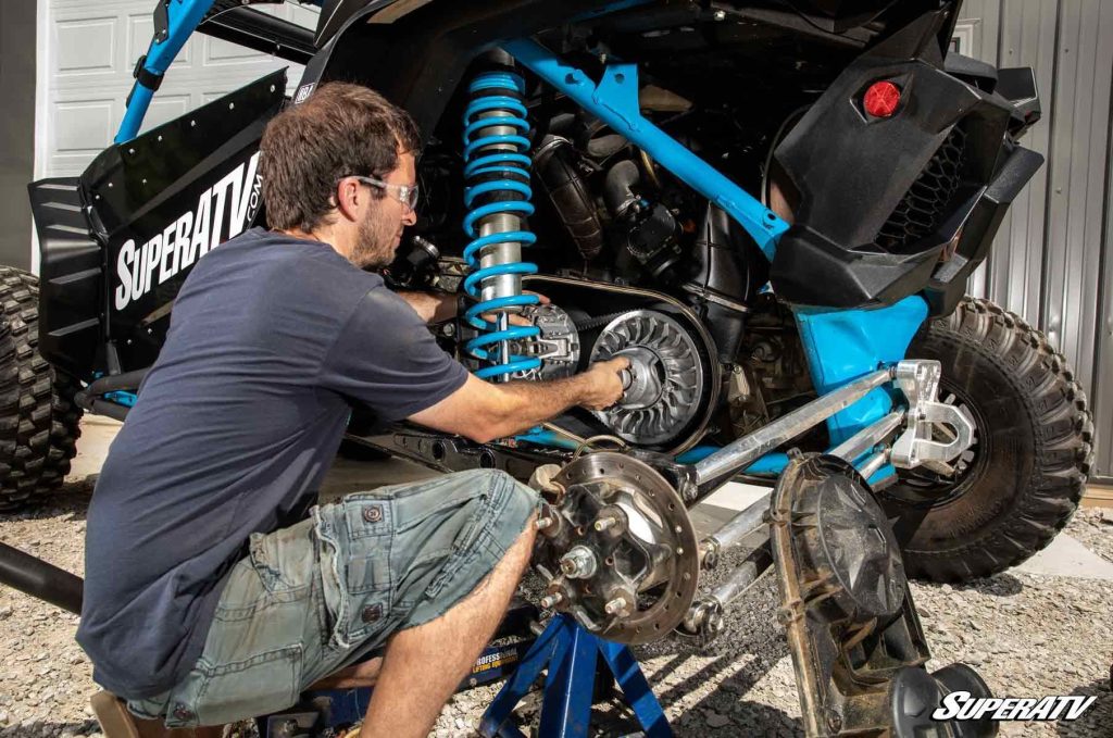 A man crouched with one hand on the secondary clutch of a Polaris RZR.