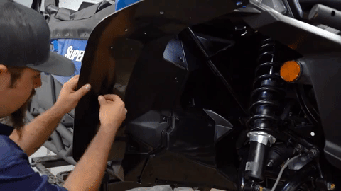 Braden uses his thumb to insert a push pin through the holes he drilled. Once installed, the push pin holds the fender flare in place.