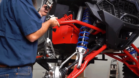 Braden lifts the upper A-arm up and attaches it to a strap.