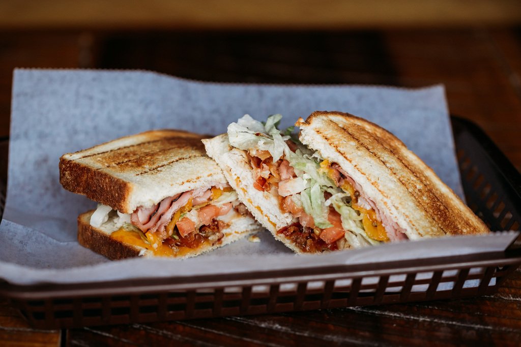 A panini cut in half featuring roasted turkey, bacon, cheese, tomato and lettuce. It looks crunchy and flavorful.