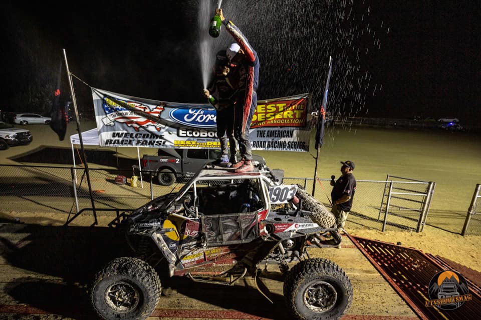 Racers standing on top of buggy clebrating win with champagne