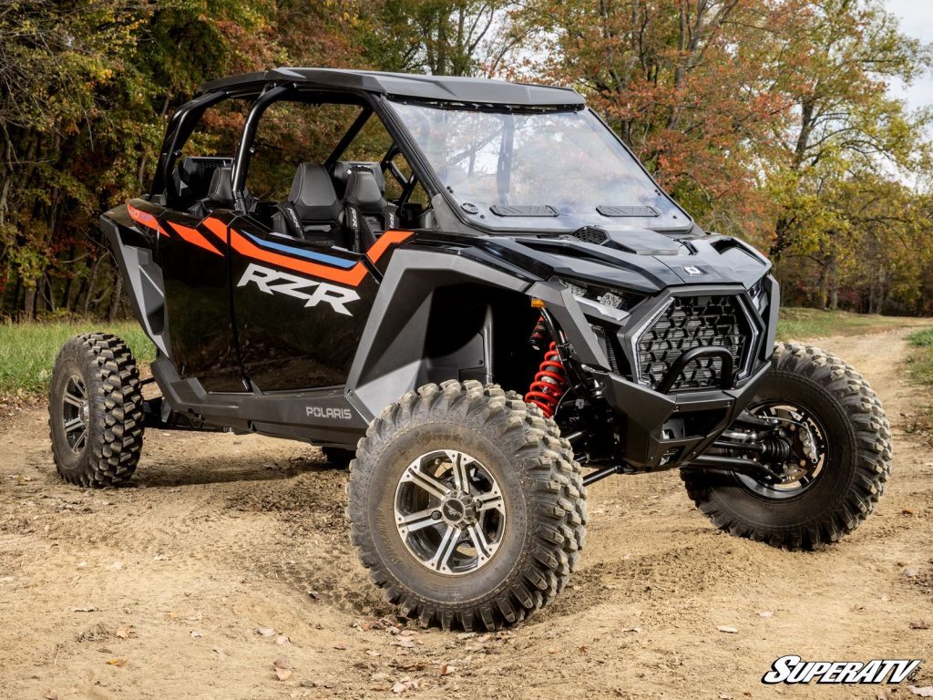 A Polaris RZR parked on a dirt path with a vented polycarbonate windshield installed.