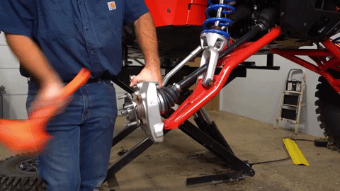 Braden beats the axle with a bright orange mallet.
