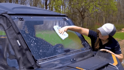 A woman wiping a wiping an UTV windshield in long swipes.