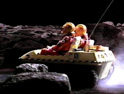 Two people in space suits drive an Amphicat across a moonscape.