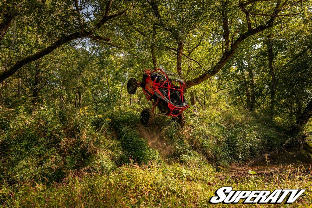 A RZR with portals installed racing up the side of a short hill and popping a wheelie.