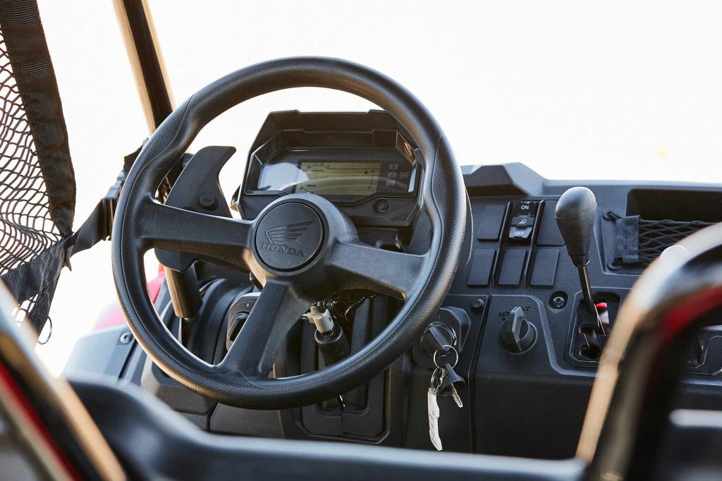 The dashboard of a Honda Pioneer. The keys are in the ignition and the Honda logo is emblazoned in the middle of the steering wheel.