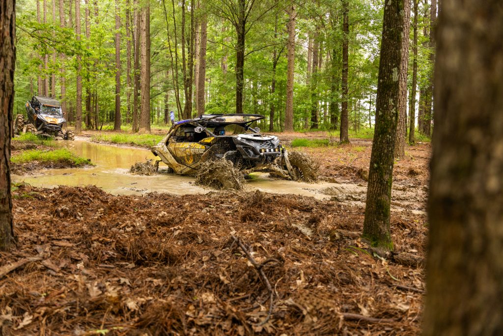 UTV driving through a mud hole on a wooded trail.