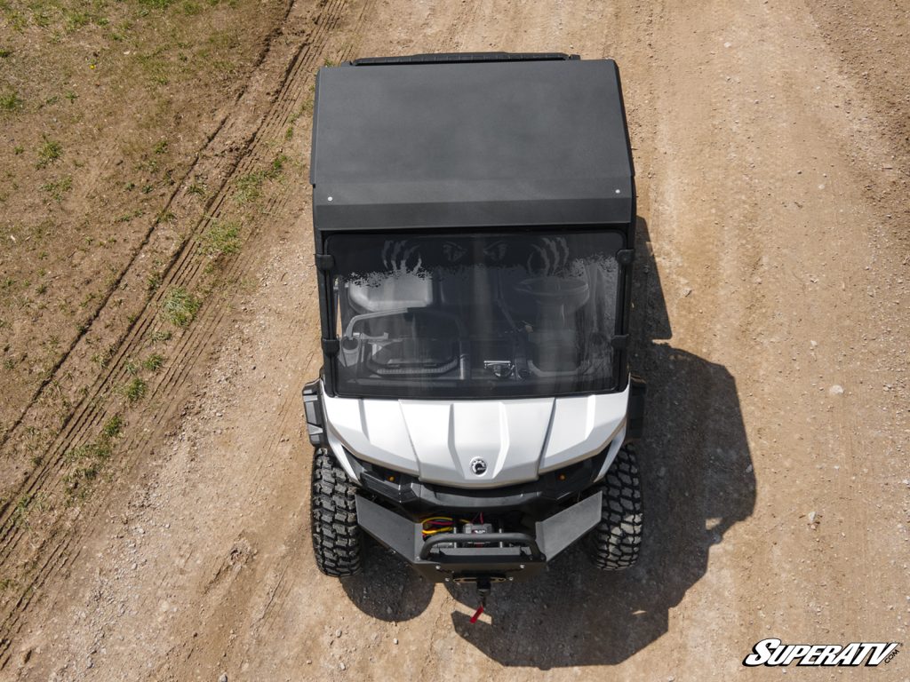 A white Can-Am Defender with a black aluminum roof rolling down a dirt road.