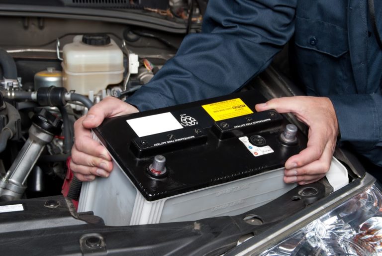 A person removes a car battery from its location inside the car.