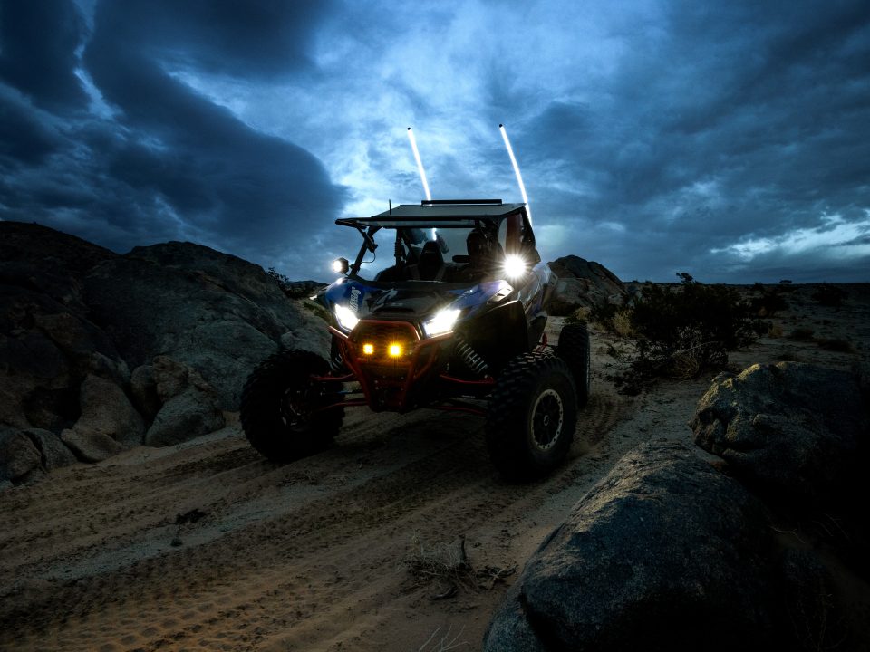 UTV at night coming over a small hill with its headlights and auxiliary lights on.