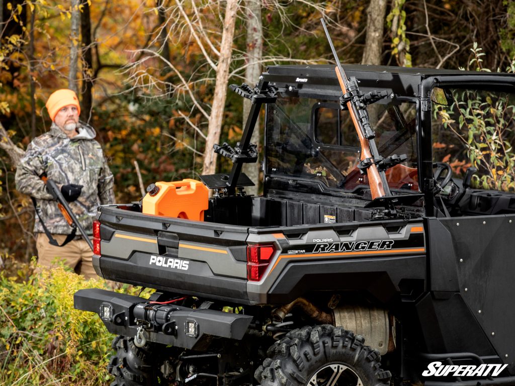 A man walking towards a Polaris Ranger with an in-bed gun rack.
