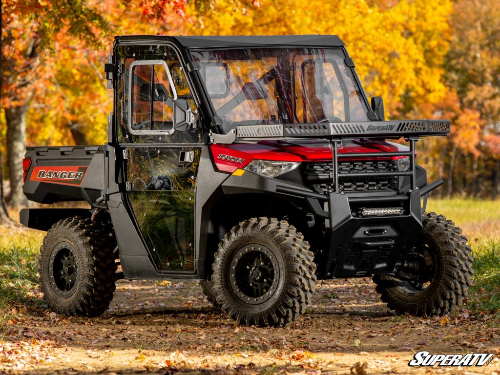 A Polaris Ranger with a full cab enclosure in front of a lush fall background.
