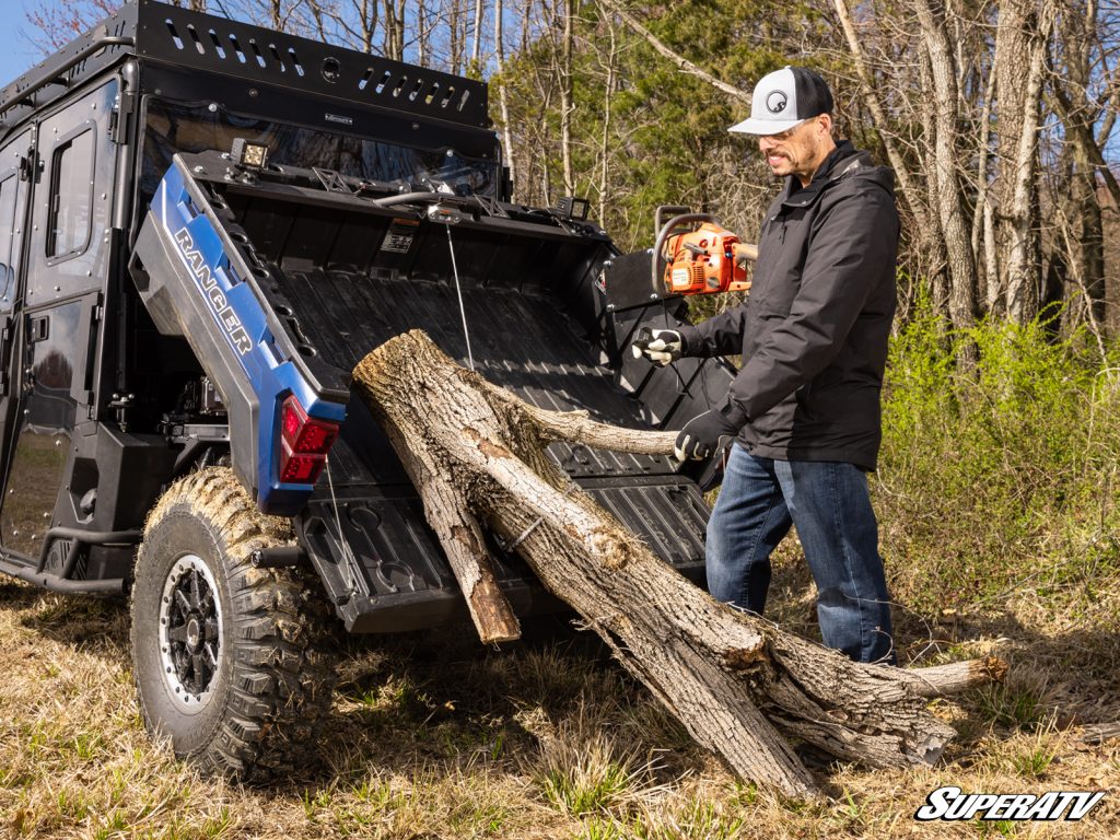 A man using a bed winch to pull a log into his Ranger's dump bed.