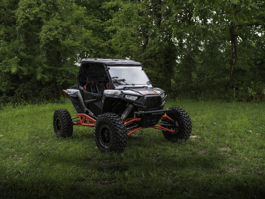 Polaris RZR sitting in a field with trees in the background.