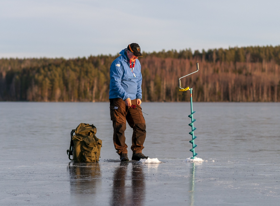A person Ice fishing with a hand auger and gear