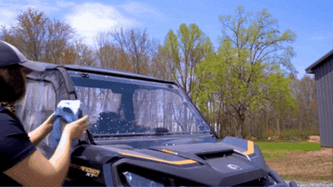 A woman using a microfiber cloth to clean a UTV windshield.
