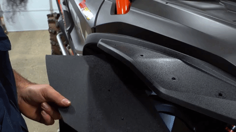 A person drills a hole up through the fender flare.