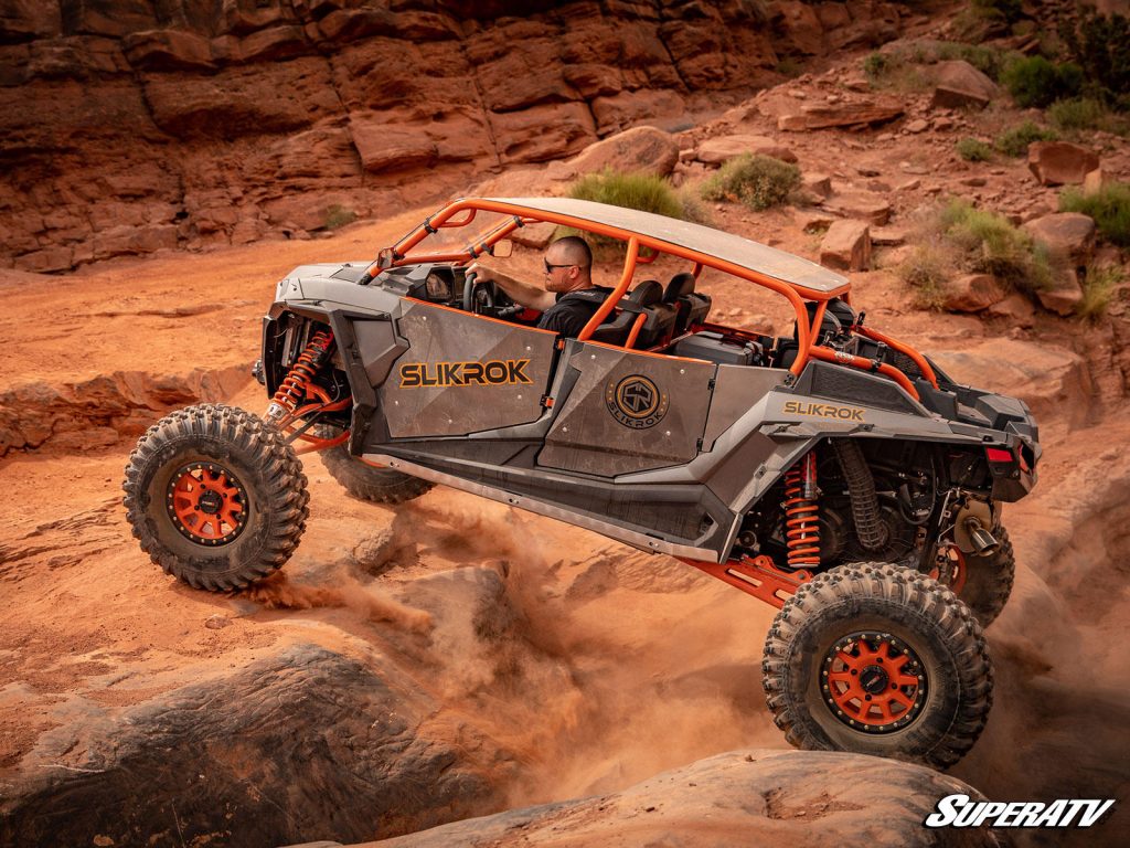 A UTV with all-terrain tires taking on a dusty, rocky climb.