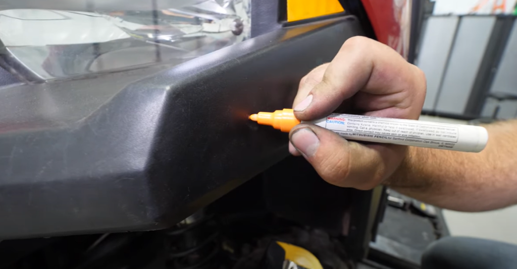 A person using an orange paint marker to indicate spots to drill