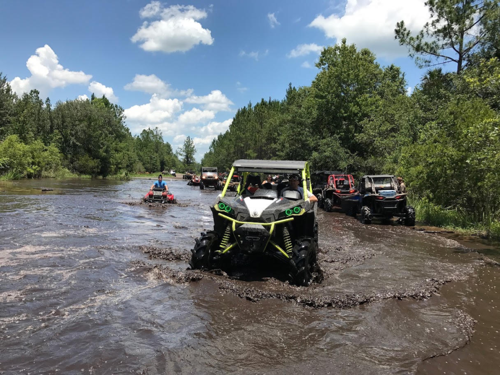 A convoy of vehicles crossing muddy water at Hog Waller Mud Bog and Park