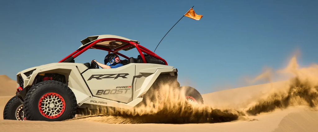 A Polaris RZR Pro R Boost ripping in the desert and throwing up a rooster tail