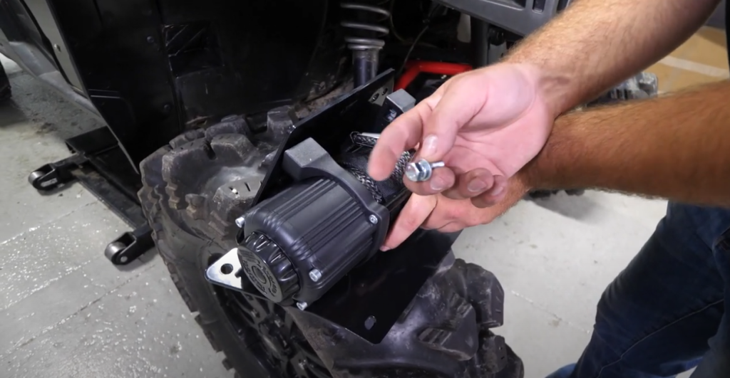 Braden holding a bolt in one hand while he rests a the winch he's installing on the Ranger's tire.