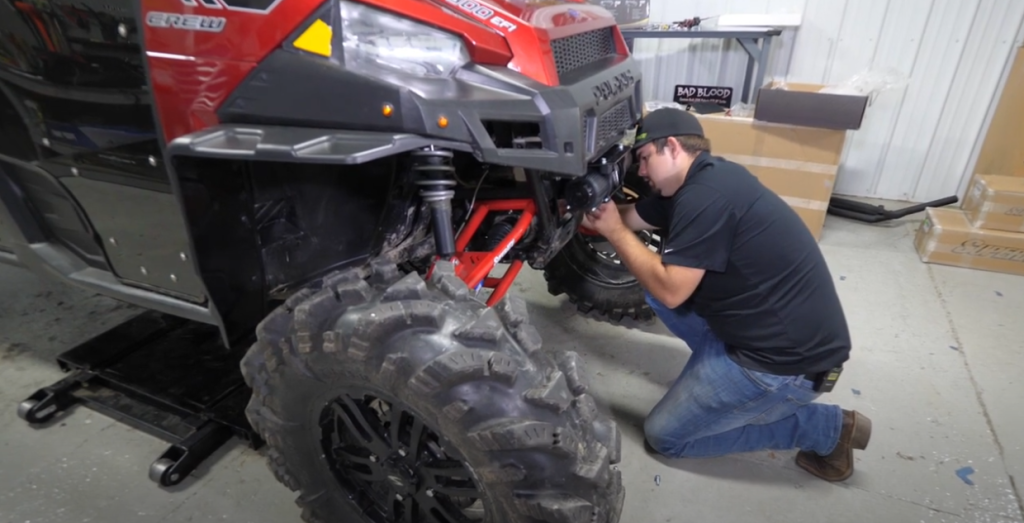 Braden reaching behind the winch on his knees to tighten the bolts.