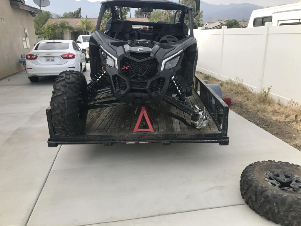 A Can-Am Maverick X3 sitting on a trailer with broken suspension.
