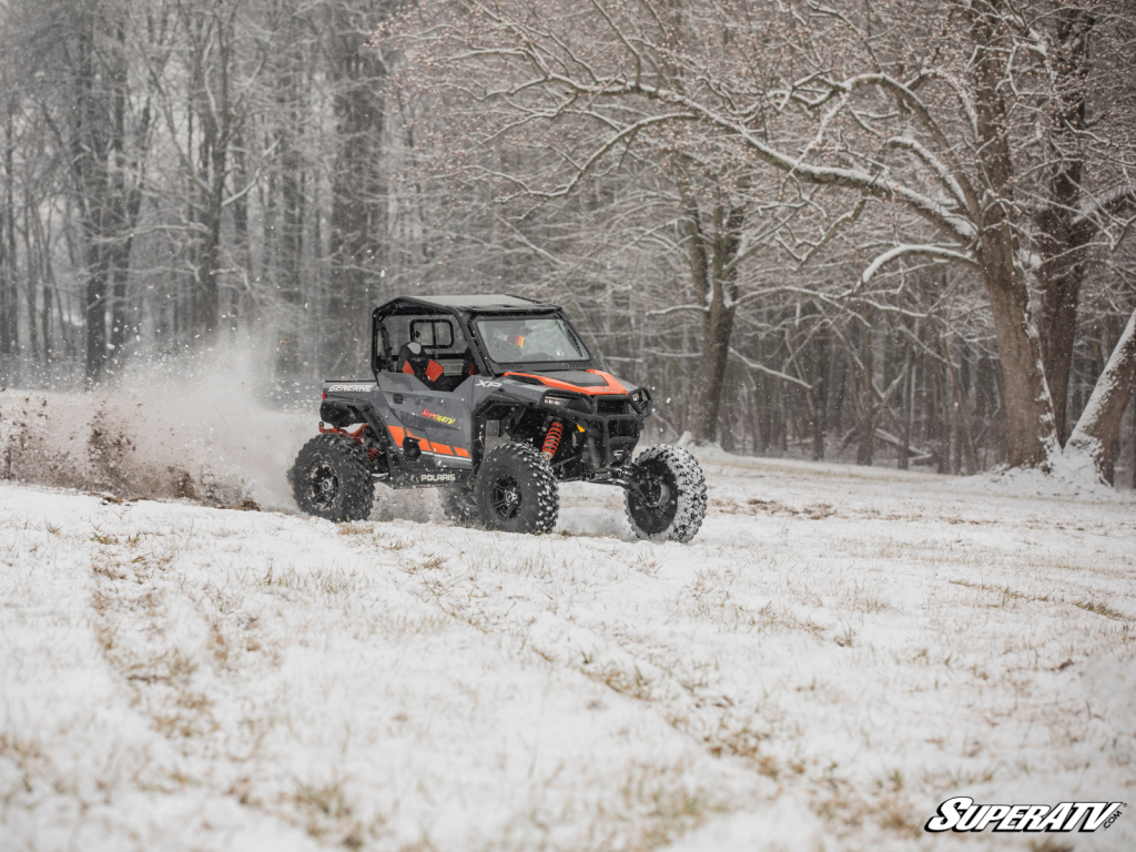 An organge and grey UTV racing across a snow-covered field.