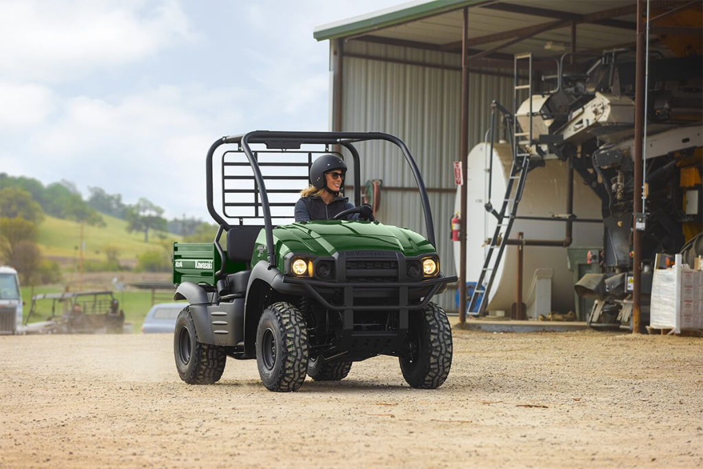 A woman drives a Kawasaki Mule past a pole barn.