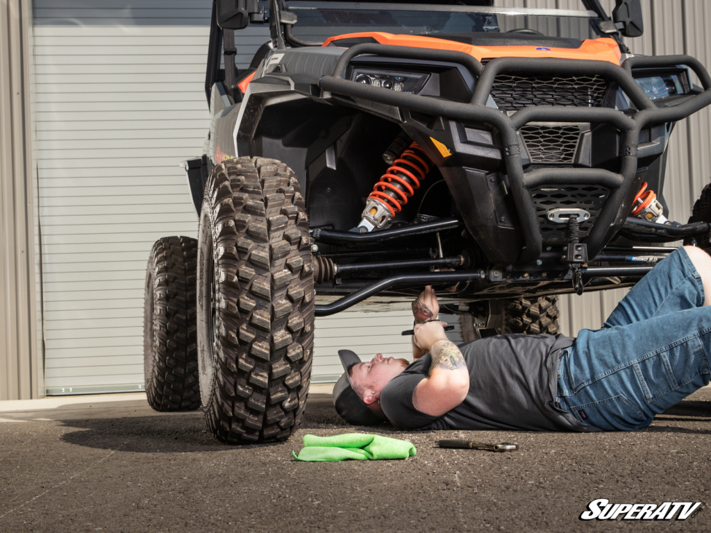 A young man lays on the ground under a UTV doing work on the machine.