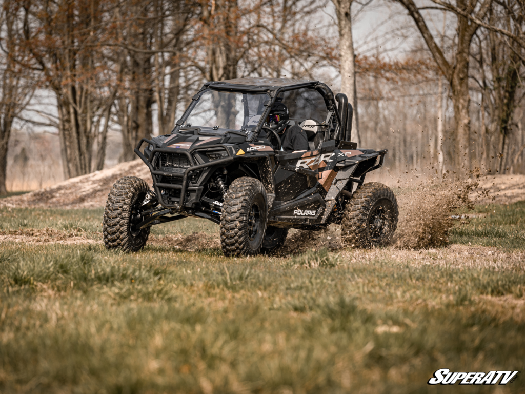 A Polaris RZR kicking up a major rooster tail as it races through a field.