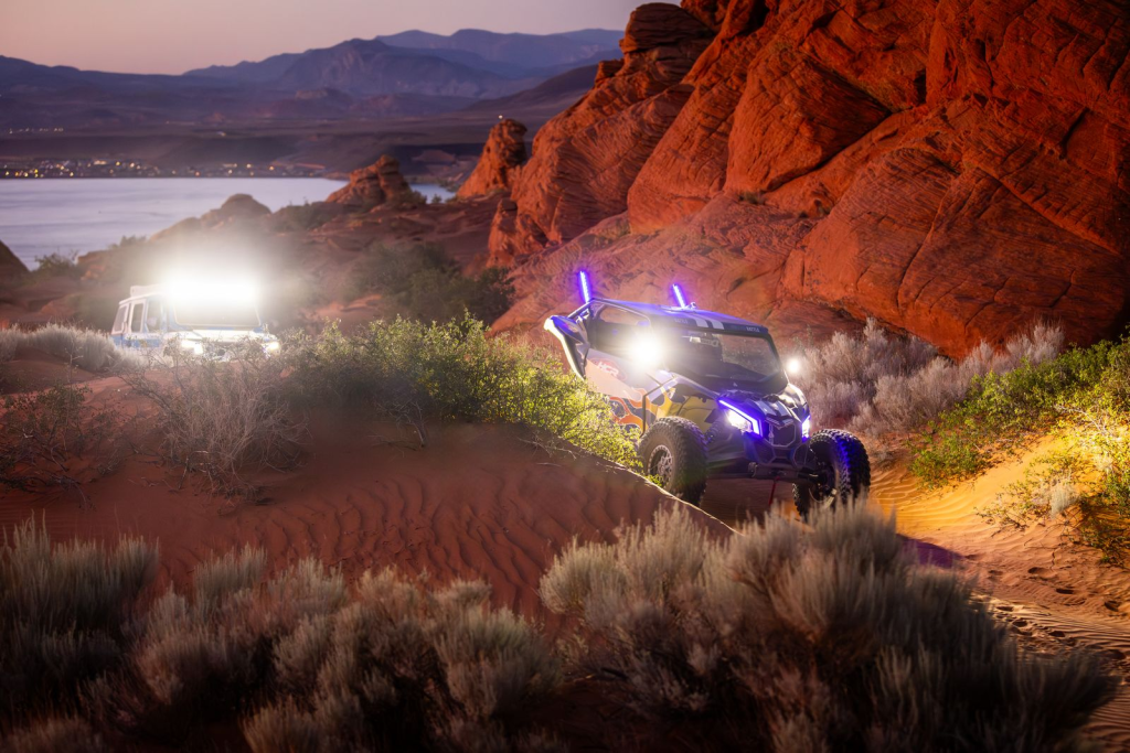 Two UTVs riding through dunes with SuperATV Whip Lights installed.