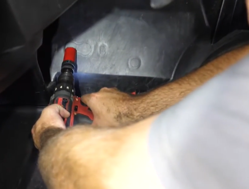 A mechanic drilling firewall holes to install grommets.