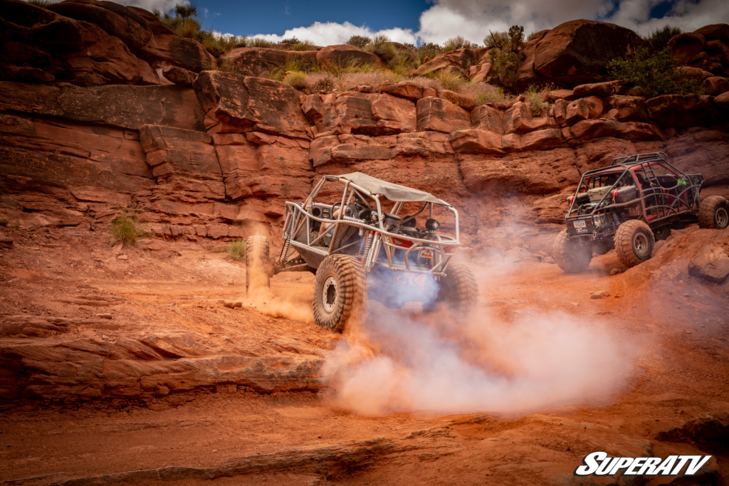 A custom rock crawler side-by-side climbing a rock shelf in Moab.