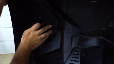 One hand holds the fender flare in place while the second hand pushes a plastic push pin through the bottom of the fender flare into the OEM fender.