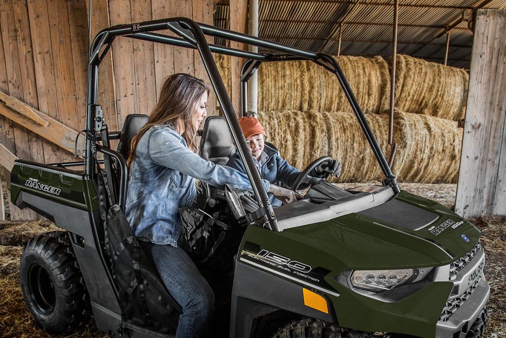 Mom and child setting up parental controls on Polaris Ranger in hay barn