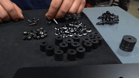 A pair of hands sorts different nuts, bolts, spacers, and washers on a table.