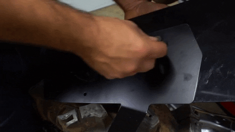 A person installs a large rectangular bracket into the underside of the fender flare.